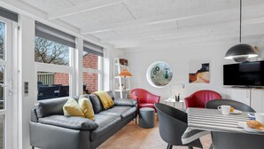 A modern living room with a grey leather sofa, red chairs, a round table with a striped tablecloth, and a TV mounted on the wall. - Beautiful home in Hemmet with WiFi (Hemmet)