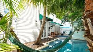 A pool area with a hammock, palm trees, and a covered patio with outdoor furniture. - Old Town Caribbean Estate Key West -  Great for Groups - Private Pool - Sleeps 21 (Key West)