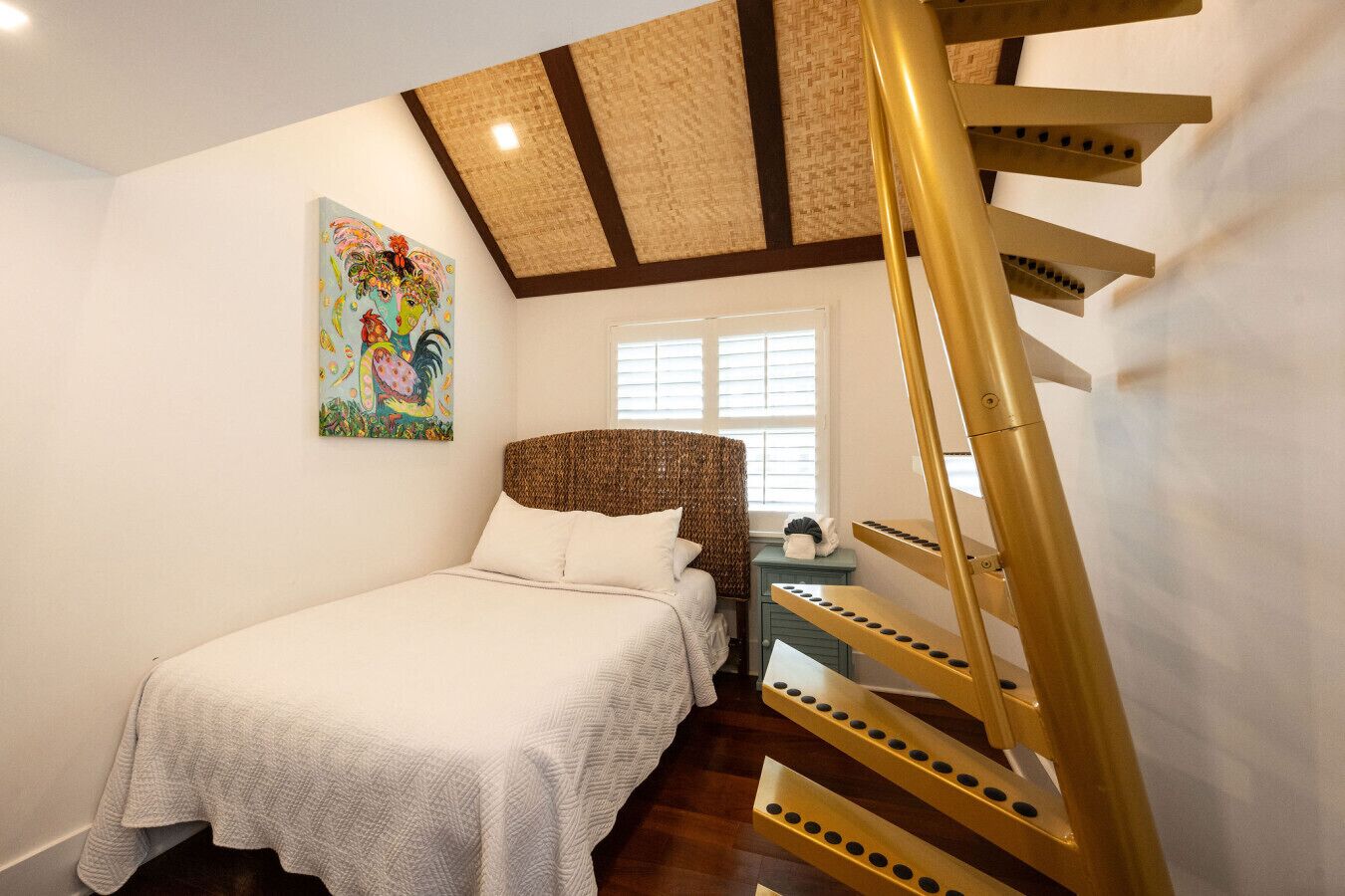 A bedroom with a bed, a painting, a window, and a staircase.