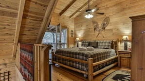 A wooden cabin bedroom with a bed, two bedside lamps, a ceiling fan, and a window. - Reeling 'Em Inn by Mountain Oasis | Fightingtown Creekfront (McCaysville)