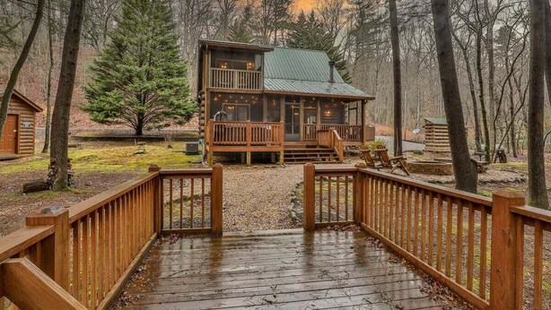 A cabin with a wooden deck, a covered porch, and a view of the surrounding forest. - Reeling 'Em Inn by Mountain Oasis | Fightingtown Creekfront (McCaysville)