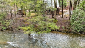 A forested area with a stream, wooden structures, and a clear path. - Reeling 'Em Inn by Mountain Oasis | Fightingtown Creekfront (McCaysville)