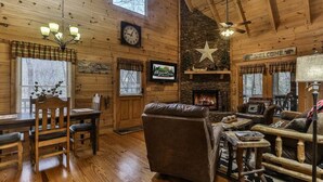 A cozy cabin interior with a wooden interior, a fireplace, a clock, and a television. - Reeling 'Em Inn by Mountain Oasis | Fightingtown Creekfront (McCaysville)