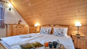A cozy bedroom with a wooden ceiling, a large bed with floral pillows, bedside lamps, and a tray with books, mugs, and a lantern. - Gorgeous home in Huba with house a mountain view (Huba)