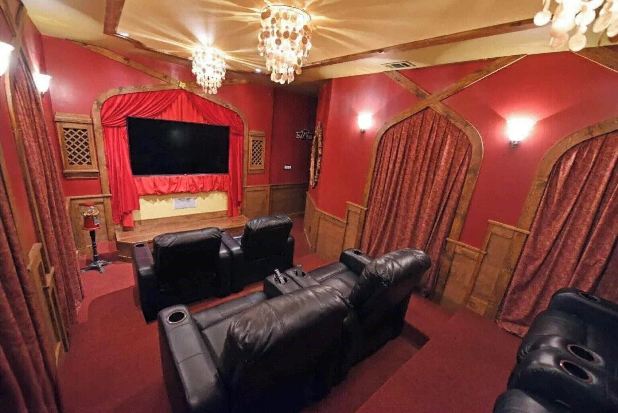 Een bioscoopzaal in huis met rode muren, een groot scherm en zwarte leren zitplaatsen.