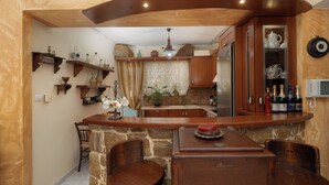 A kitchen with wooden cabinets, a stone countertop, and a dining area with two chairs. - Helena's Home (Markopoulo Mesogaias)