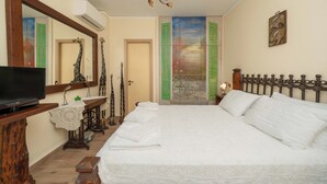 A bedroom with a large bed, a television on a wooden stand, a mirror, and a chandelier. - Helena's Home (Markopoulo Mesogaias)