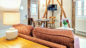 A cozy room with a brown sofa, a wooden table, a TV mounted on a wall, and a window with curtains.