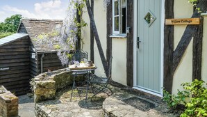 A quaint cottage named Willow Cottage with a stone bench, a table with a tray, and a door with a sign.