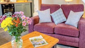 A living room with a purple sofa, a wooden coffee table, and a vase of flowers.