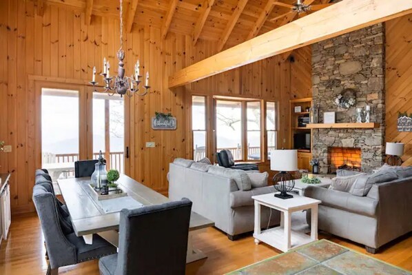 Un intérieur en bois comprenant un coin repas, des canapés, une cheminée et de grandes fenêtres.