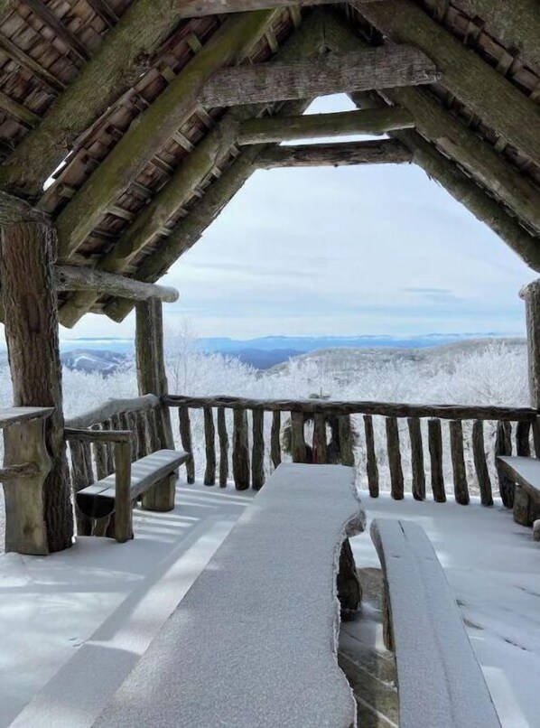 Enjoy panoramic views of snow-covered hills from this rustic lookout point, featuring a bench and table.