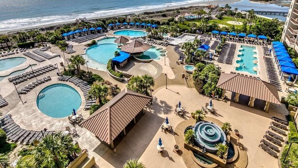 A resort with multiple swimming pools, sun loungers, and a view of the beach.