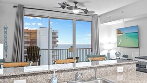 A modern kitchen with granite countertops, stainless steel sinks, and a large window offering a view of the ocean and buildings. - Shores of Panama Unit 2107~3 bedroom 3 bath~Sleeps 8 (Panama City Beach)