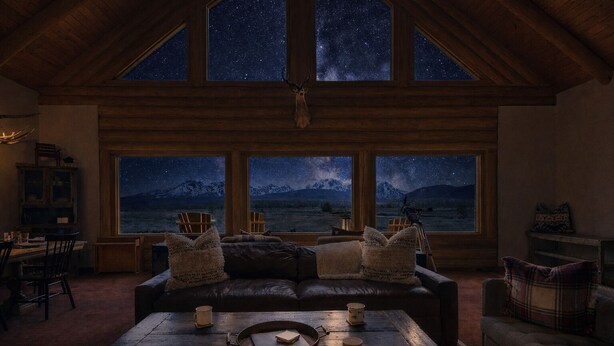 Un salon chaleureux avec une grande fenêtre donnant sur un ciel étoilé et des montagnes.