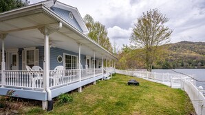 Une maison à deux étages avec une véranda et une clôture blanche qui longe le bord du lac.
