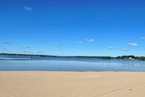 A beach with a clear sky, calm water, and distant shoreline. - Well Appointed Home Steps to Pewaukee Lake (Pewaukee)