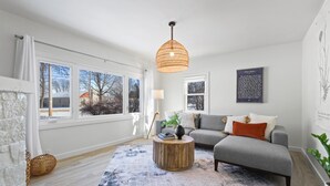Un salon moderne avec un canapé gris, une table basse ronde en bois et une grande fenêtre donnant sur un paysage enneigé.
