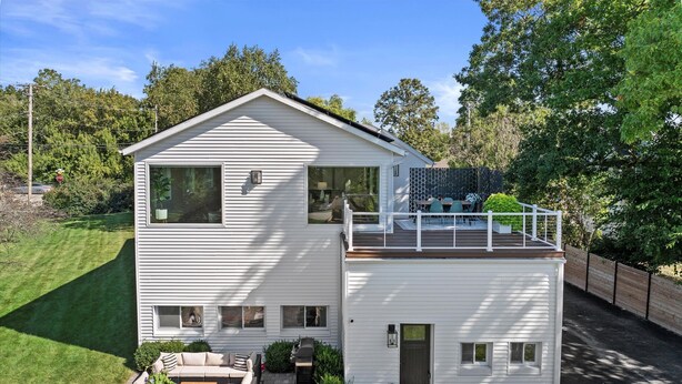 Une maison moderne à deux étages, dotée d’un balcon, d’une terrasse avec mobilier d’extérieur et d’une pelouse bien entretenue.
