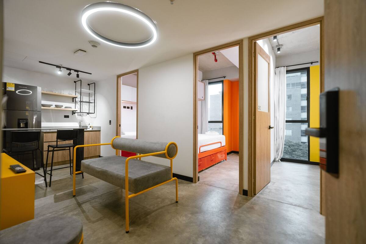 A modern, well-lit room with a kitchenette, a dining area, and a bed.
