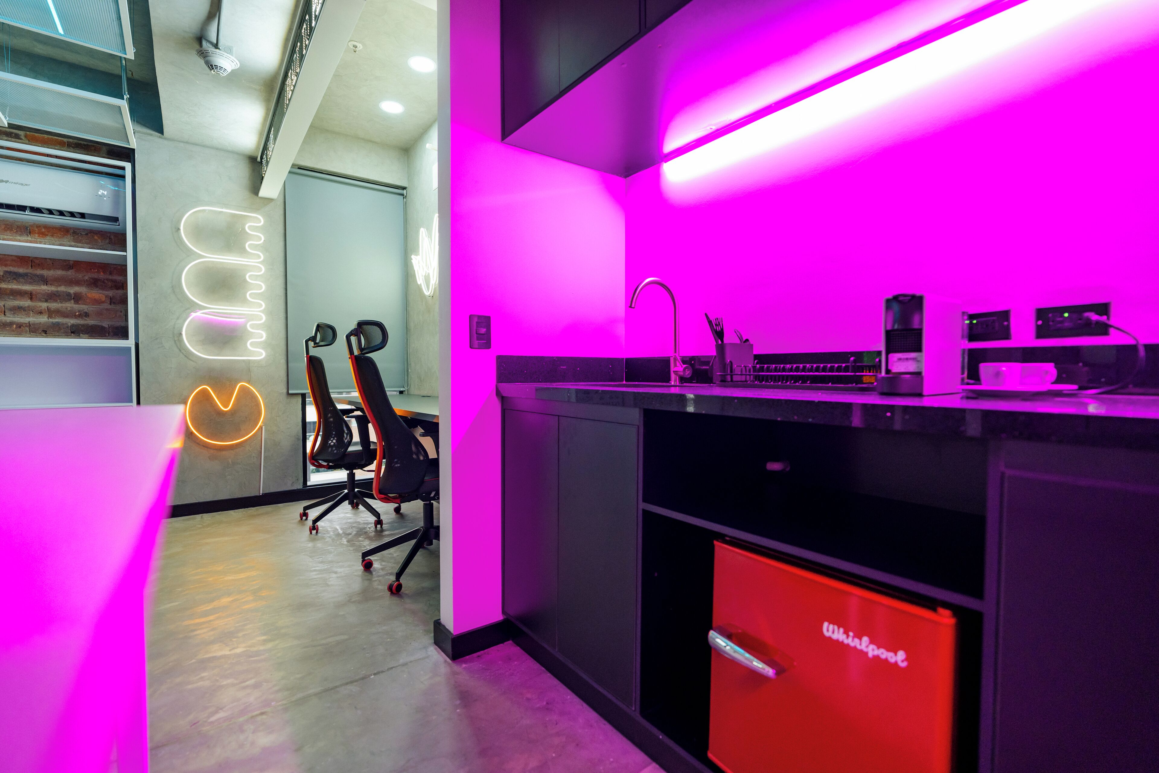 Une cuisine moderne avec un lave-vaisselle Whirlpool rouge, un plan de travail noir et un néon mural.