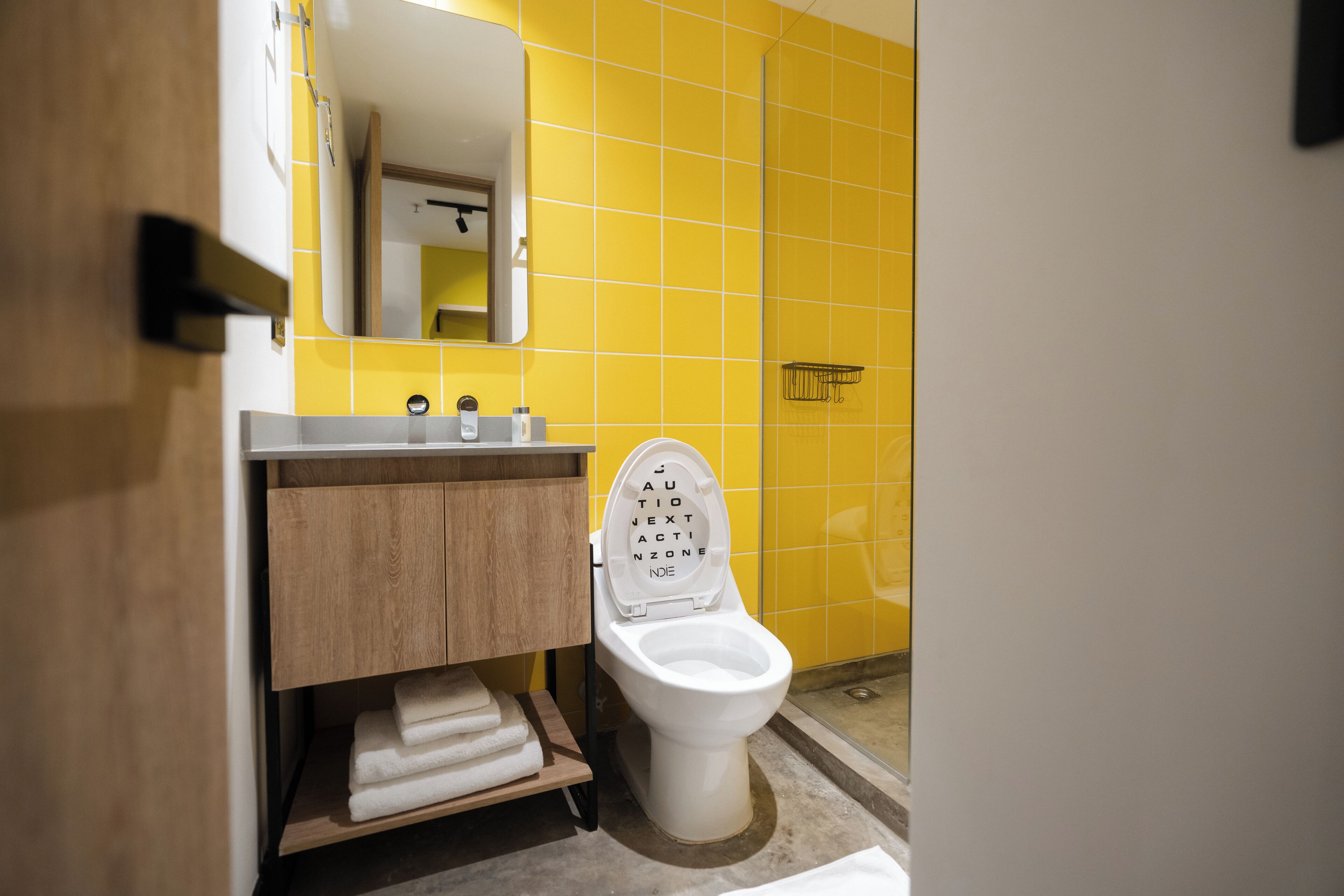 A bathroom with a white toilet, a wooden vanity, and a yellow tiled wall.