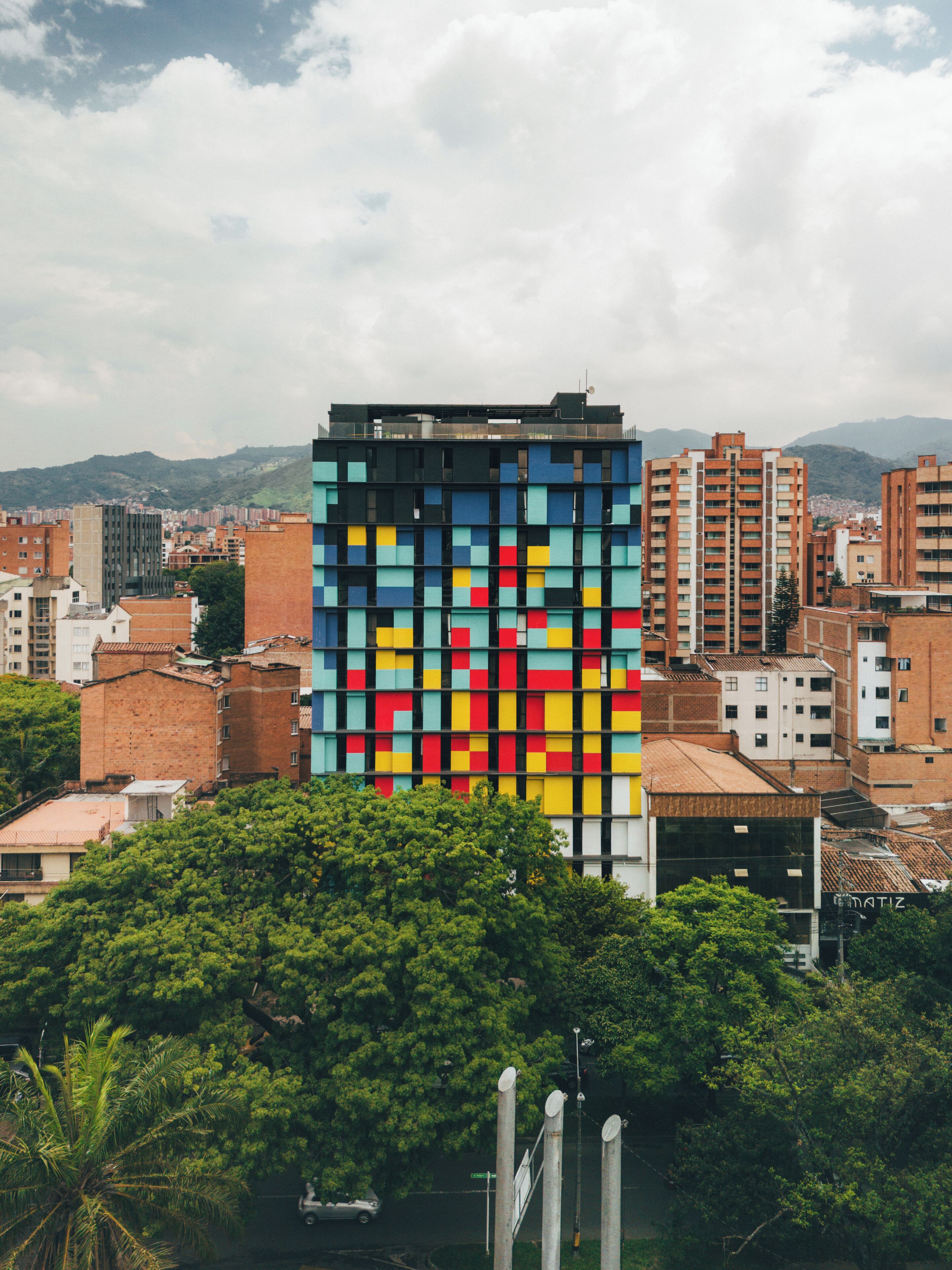 A modern building with a colorful facade, surrounded by other residential and commercial structures, and a lush green area in the foreground.