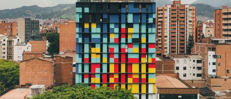 A modern building with a colorful facade, surrounded by other residential and commercial structures, and a lush green area in the foreground.