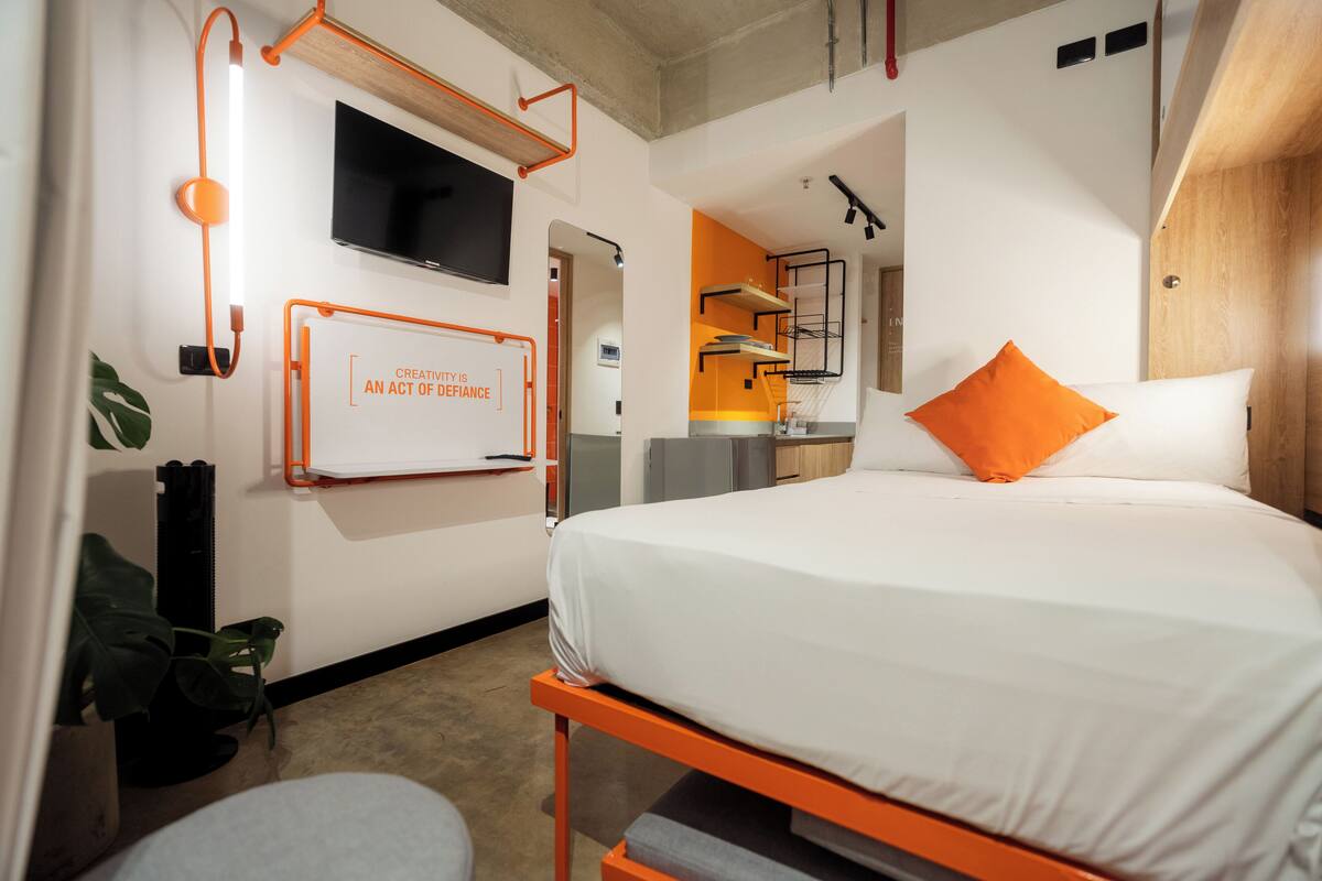 A modern hotel room with a bed, a TV mounted on the wall, and a whiteboard with motivational quote.