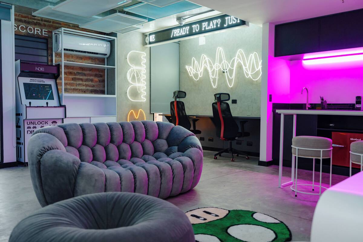 A modern office space with a bean bag chair, a neon wave design on the wall, and a sign that reads "READY TO PLAY? JUST".