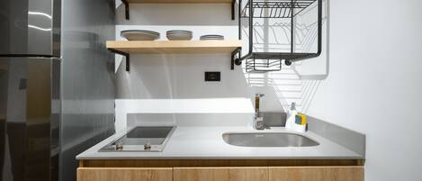 A modern kitchen with a stainless steel refrigerator, wooden cabinets, a white countertop, and a built-in sink.