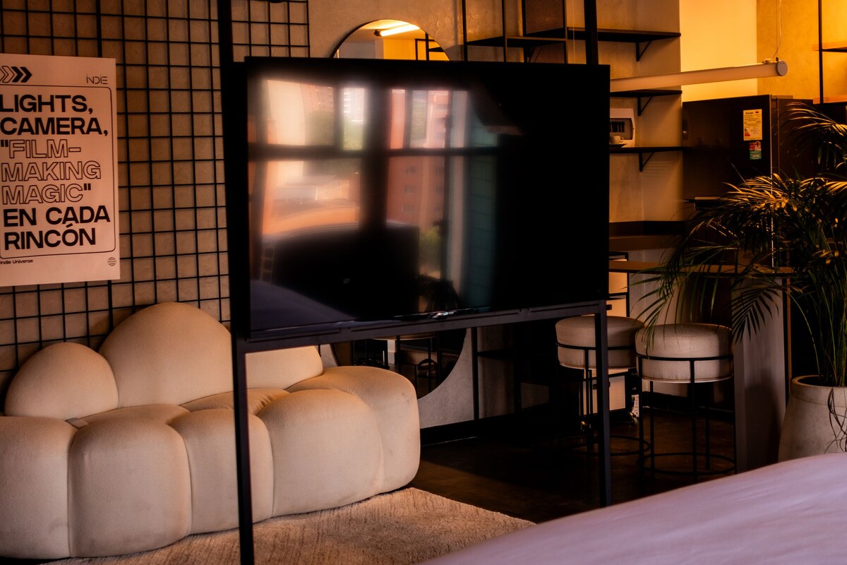 A modern hotel room with a large bed, a sofa, a TV on a stand, and a small table.