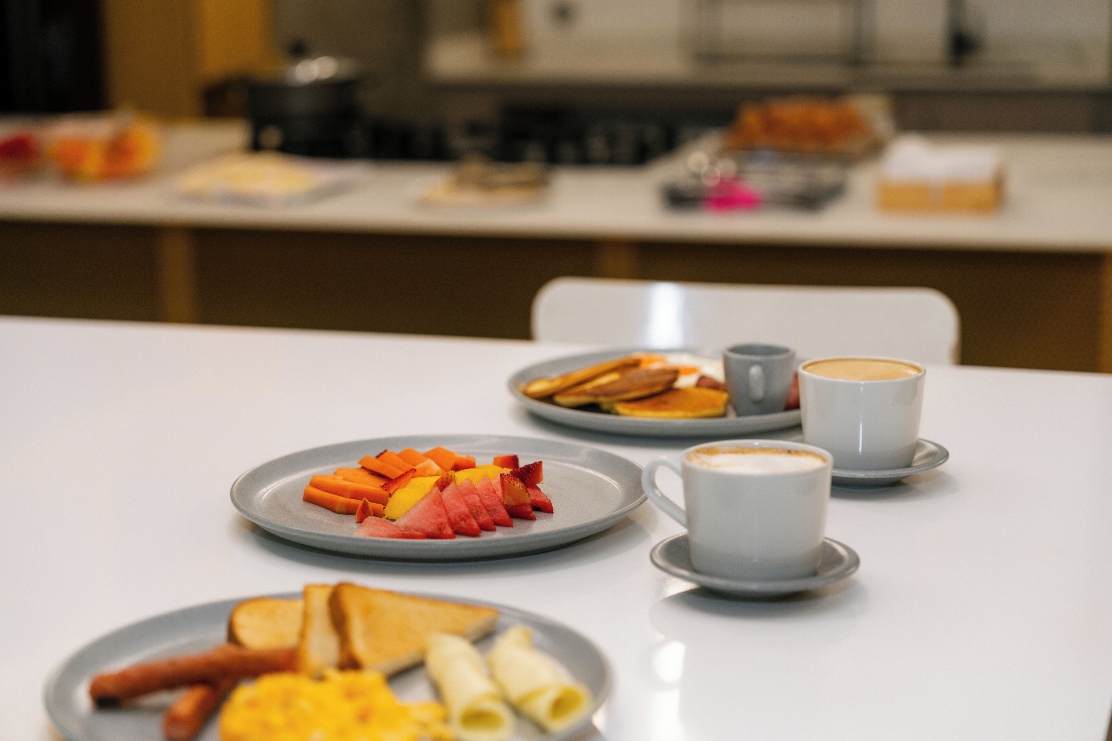 Una mesa de desayuno con platos de fruta, tostadas y huevos, y dos tazas de café.
