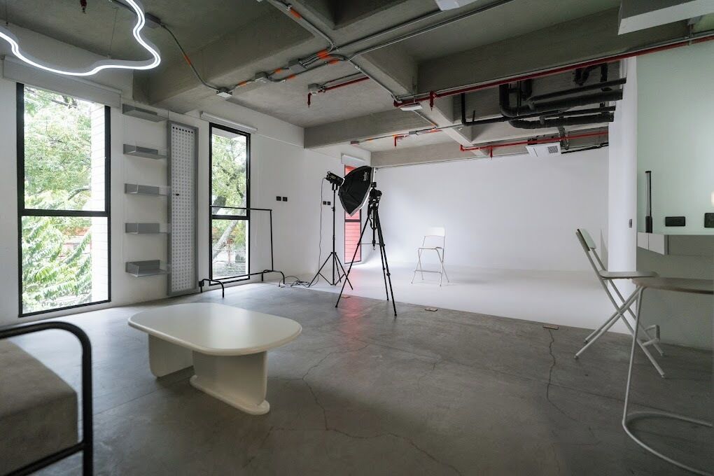 A modern, industrial-style room with large windows, a white table, and a tripod-mounted camera.