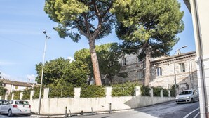 A street with a large tree, a white car, and a building with stone walls. - N213 - Numana, new apartment in the center (Numana)