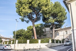 A street with a large tree, a white car, and a building with stone walls.