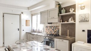 A modern kitchen with white cabinets, a tiled backsplash, and a dining area with a table covered in a transparent tablecloth. - N213 - Numana, new apartment in the center (Numana)