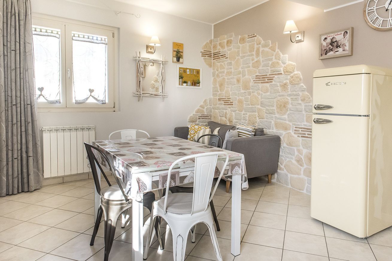 Un comedor con mesa y sillas, un sofá, un refrigerador y una pared de piedra.