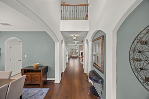 A spacious hallway with a wooden floor, a dining area with a table and chairs, and a staircase leading to an upper level.