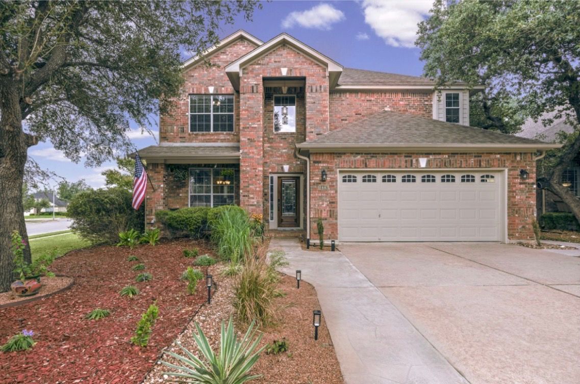 A two-story brick house with a garage, surrounded by landscaped garden beds and a flag.