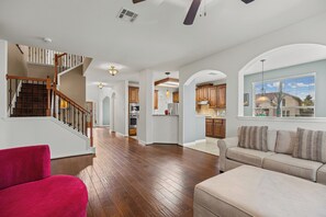 A spacious living area with a wooden staircase, a kitchen, and a dining area.
