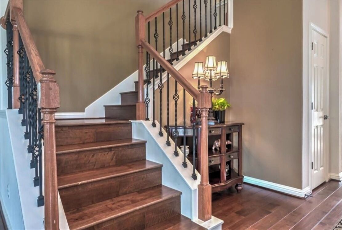 Una escalera de madera con barandilla blanca y balaustres negros, que conduce a una plataforma con una lámpara y una mesita.