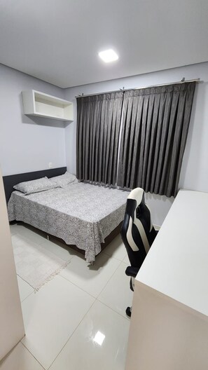 A bedroom with a bed, a desk, a chair, a window with curtains, and a ceiling light.