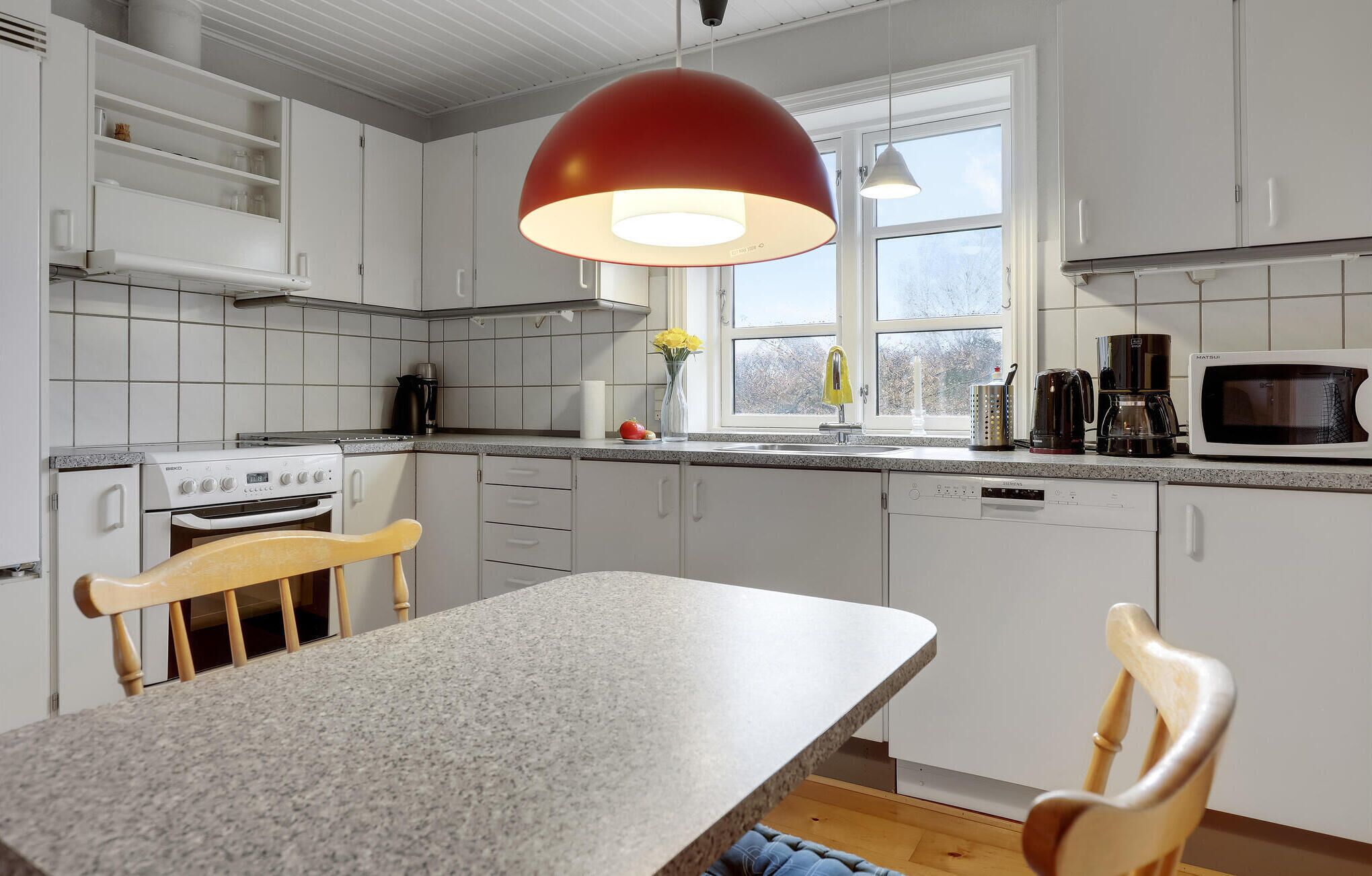 A modern kitchen with white cabinets, a granite countertop, a red pendant light, a microwave, and a stove.