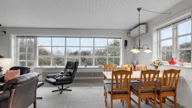 A dining area with a table and chairs, a black leather chair, a radiator, and large windows with a view of greenery. - Lovely home in Aakirkeby with WiFi (Aakirkeby)