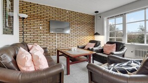 A living room with a brick wall, leather sofas, a coffee table, and a TV mounted on the wall. - Lovely home in Aakirkeby with WiFi (Aakirkeby)