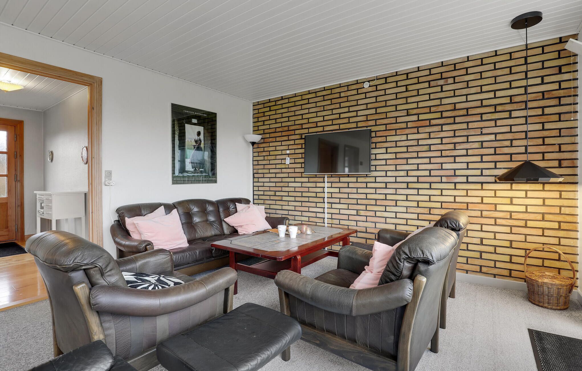 Un salon avec un mur en briques, des meubles en cuir, un téléviseur à écran plat et une porte en bois.