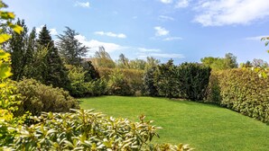 A well-maintained garden with a variety of shrubs and trees, a neatly trimmed lawn, and a clear blue sky. - Lovely home in Aakirkeby with WiFi (Aakirkeby)