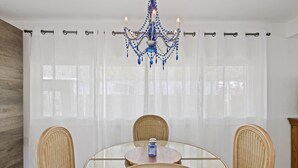 Un coin repas avec une table ronde en verre, des chaises en osier et un lustre.