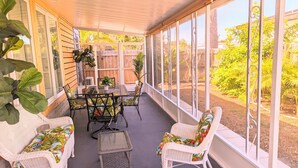 Une terrasse couverte avec une table et des chaises, de grandes fenêtres et des plantes en pot.
